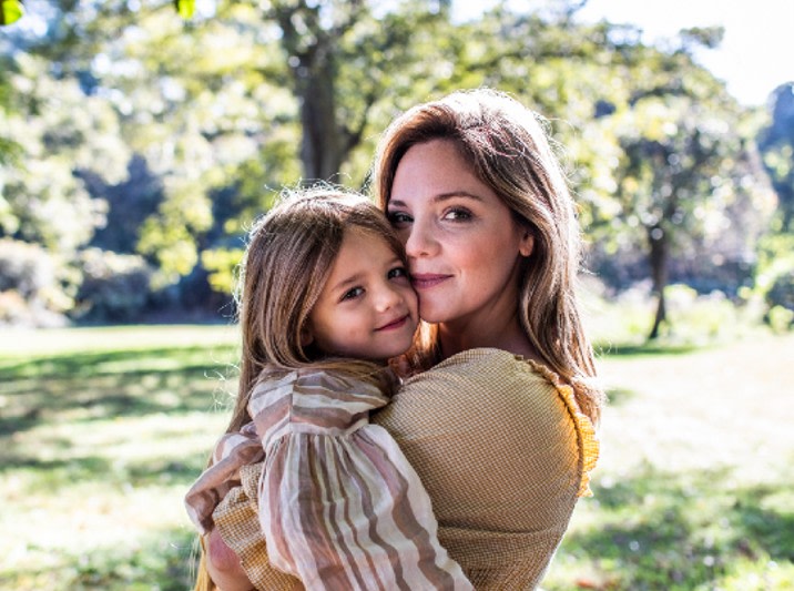 A mother holding her daughter in a park and smiling